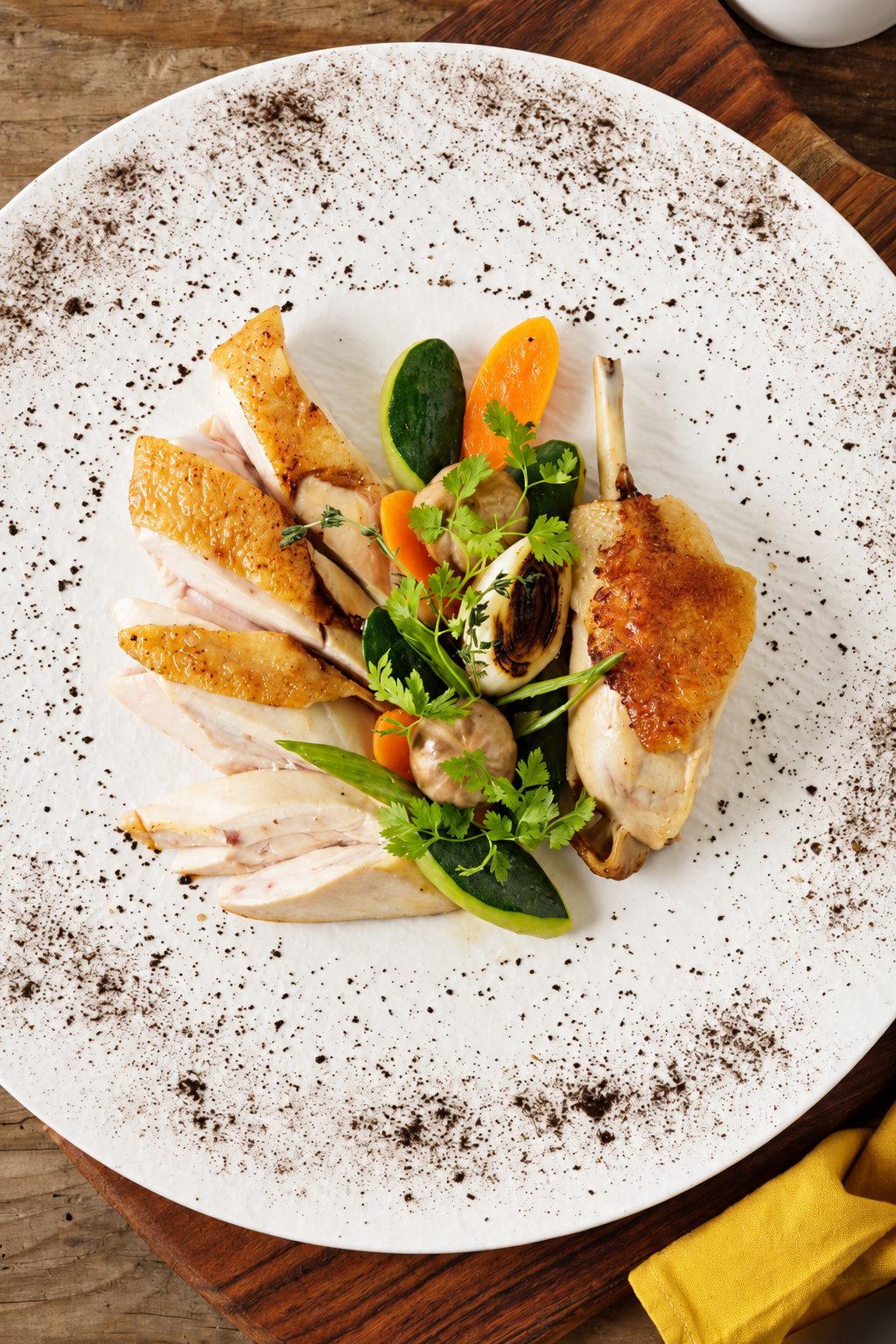 Vue de dessus d'une assiette blanche mouchetée contenant des tranches de volaille rôtie, une cuisse, des rondelles de courgette et de carotte, des oignons et du cerfeuil.