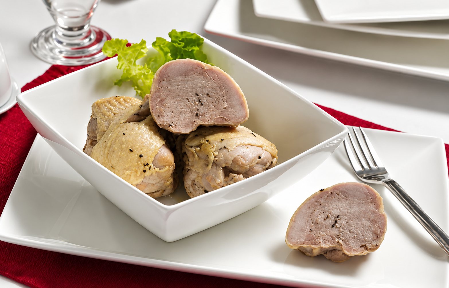 Des cuisses de volaille farcies et une moitié tranchée sont servies dans un bol carré blanc, avec une feuille de salade, une fourchette et une assiette sur un set de table rouge.